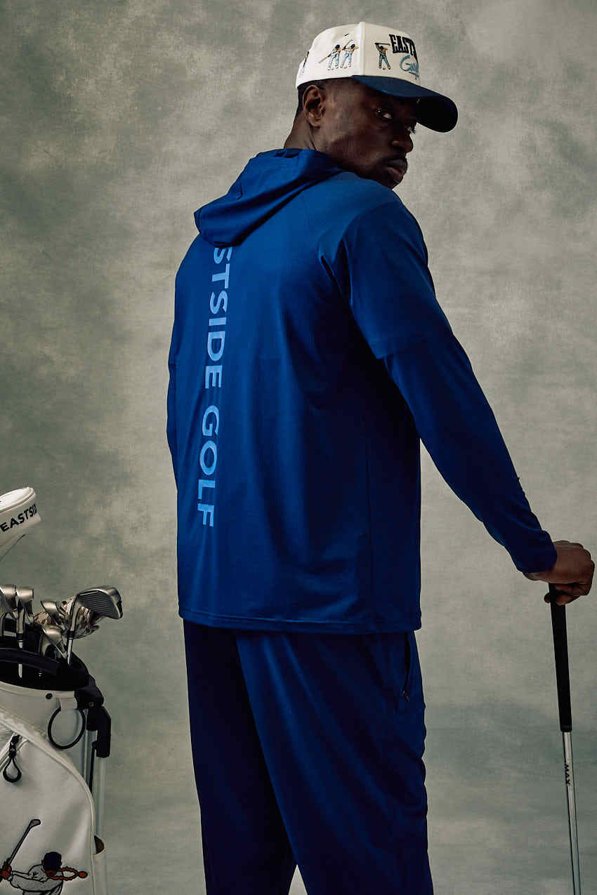 Person wearing a blue 'Eastside Golf' outfit holding a golf club with a neutral background